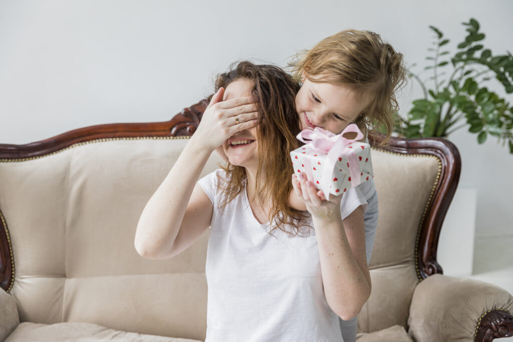 Mother covering her eyes while receiving a beautifully wrapped gift from her child