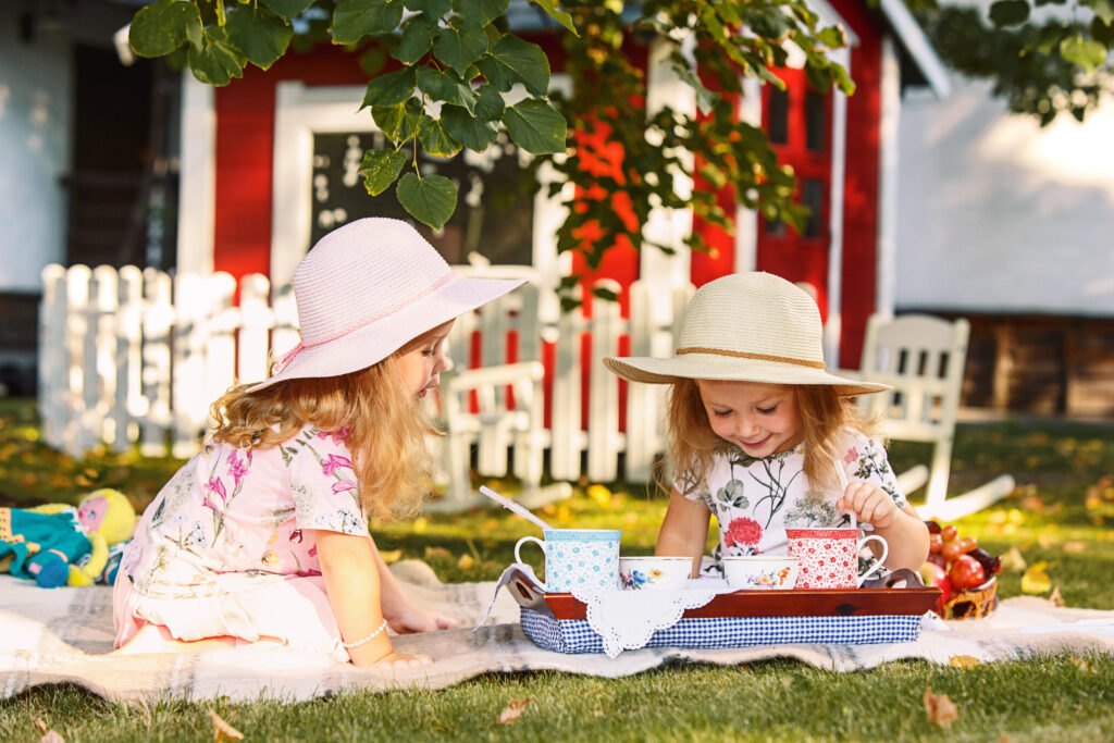Two little girls in hats having a picnic outdoors