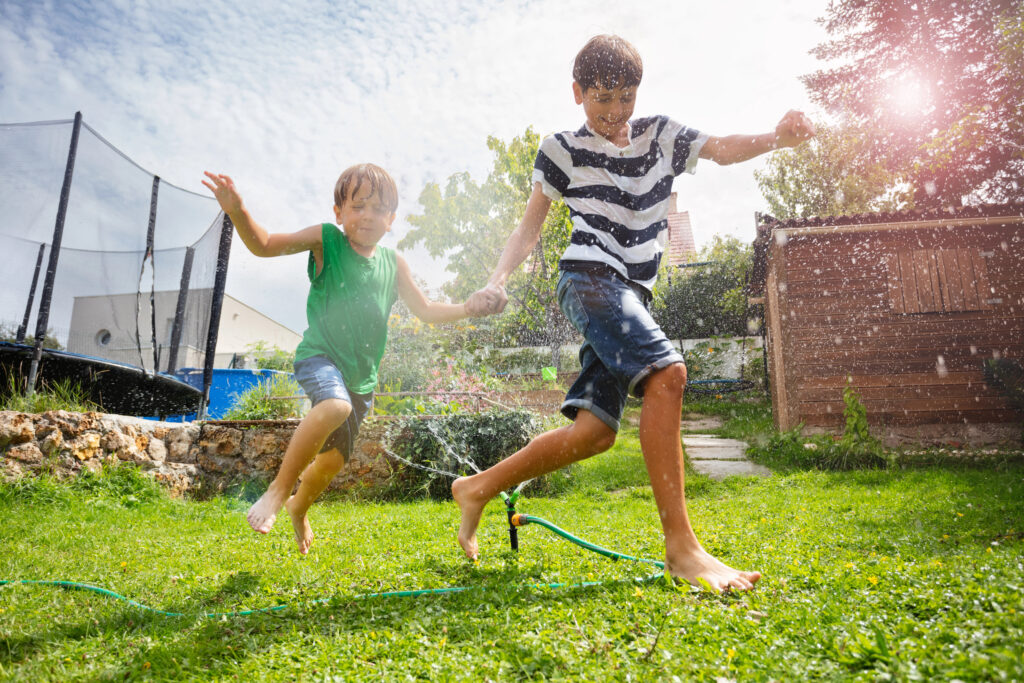 Two boys running through sprinkler outdoors